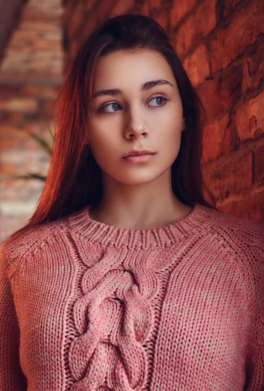 Woman in a pink sweater by a brick wall