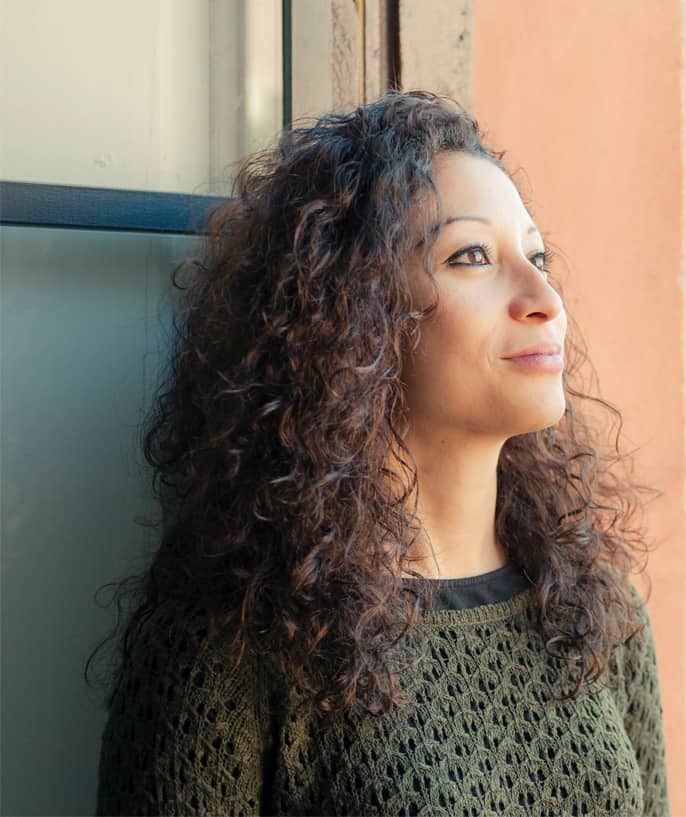 A woman wearing a green knitted sweater gazes thoughtfully