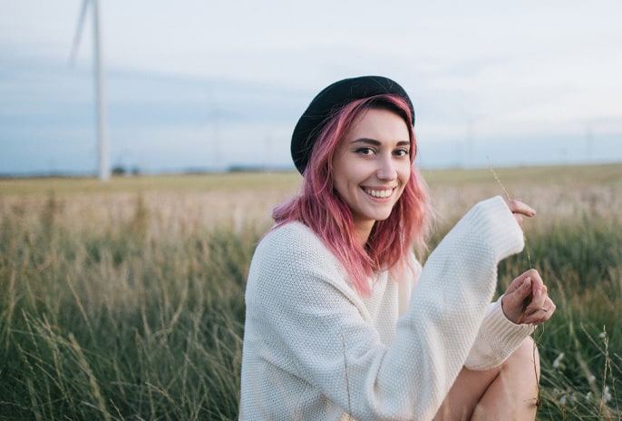 A smiling woman wearing white sweater sitting in a field